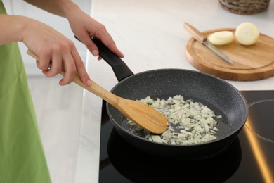 Photo of Woman frying chopped onion in kitchen, closeup