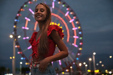 Photo of Beautiful young woman against glowing Ferris wheel in amusement park, space for text