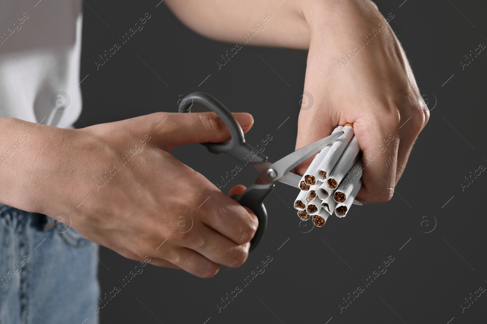 Photo of Stop smoking concept. Woman cutting cigarettes on gray background, closeup