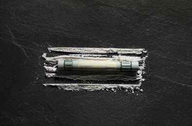 Photo of Drug addiction. Cocaine and rolled dollar banknote on dark textured background, top view