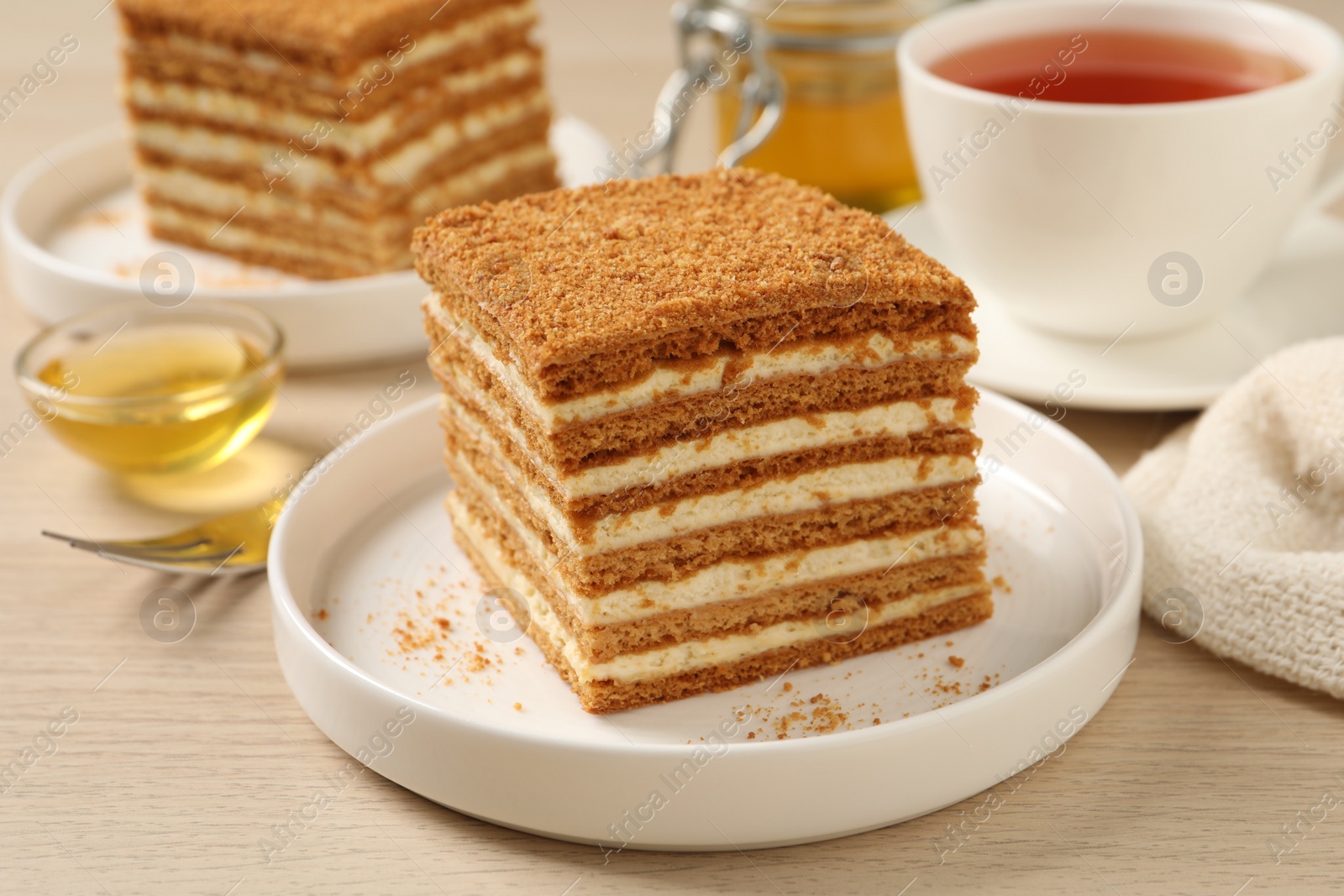 Photo of Delicious layered honey cake served with tea on wooden table, closeup