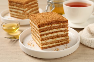 Delicious layered honey cake served with tea on wooden table, closeup