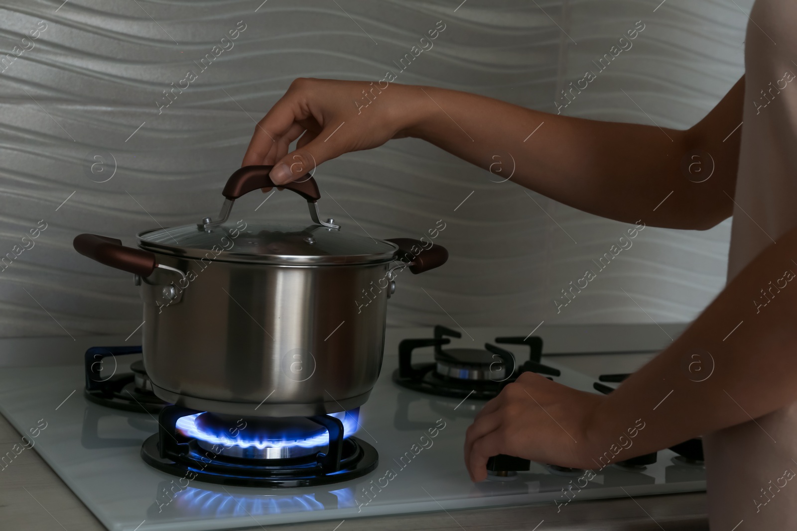Photo of Woman near gas stove with pot in kitchen, closeup