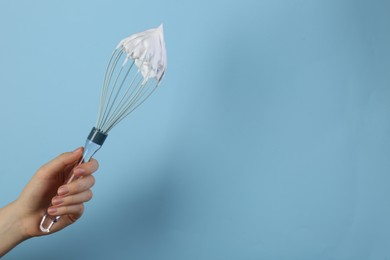 Photo of Woman holding whisk with whipped cream on light blue background, closeup. Space for text