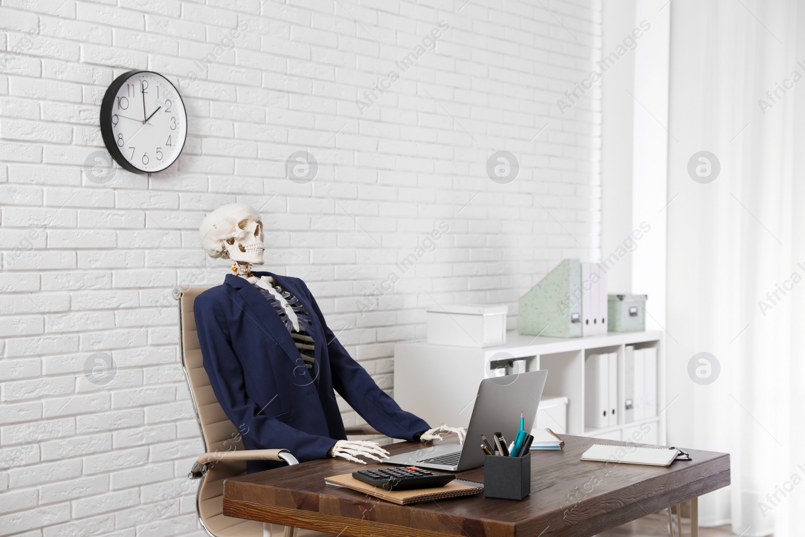 Photo of Human skeleton in suit using laptop at table in office