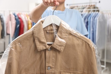 Photo of Dry-cleaning service. Woman holding shirt in plastic bag indoors, closeup