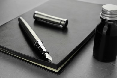 Stylish fountain pen, bottle of ink, cap and leather notebook on light grey textured table, closeup