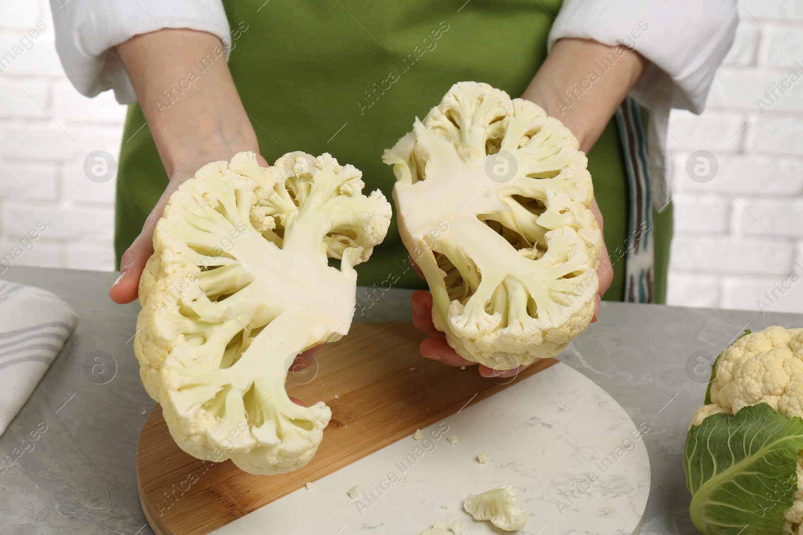 Photo of Woman holding halves of fresh cauliflower at light grey table, closeup