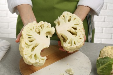 Woman holding halves of fresh cauliflower at light grey table, closeup