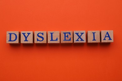 Wooden cubes with word Dyslexia on orange background, flat lay