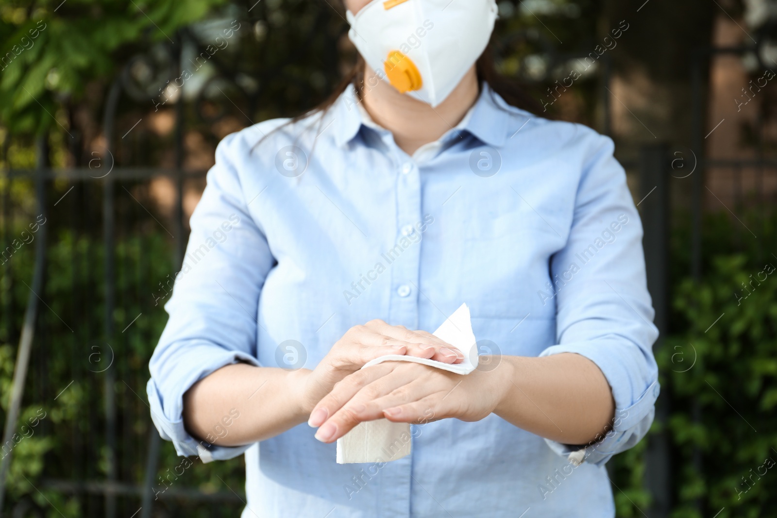 Photo of Woman cleaning hands with antiseptic wipe outdoors, closeup. Virus prevention