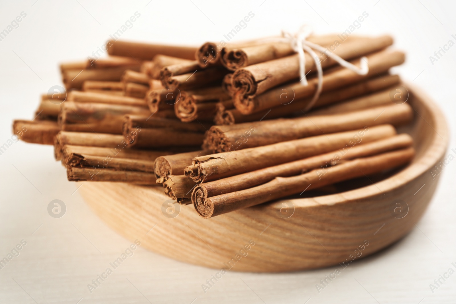 Photo of Aromatic cinnamon sticks in bowl on white wooden table, closeup