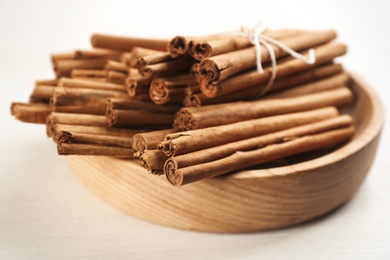 Aromatic cinnamon sticks in bowl on white wooden table, closeup