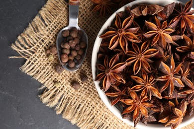 Photo of Bowl with aromatic anise stars and pepper on dark table, flat lay