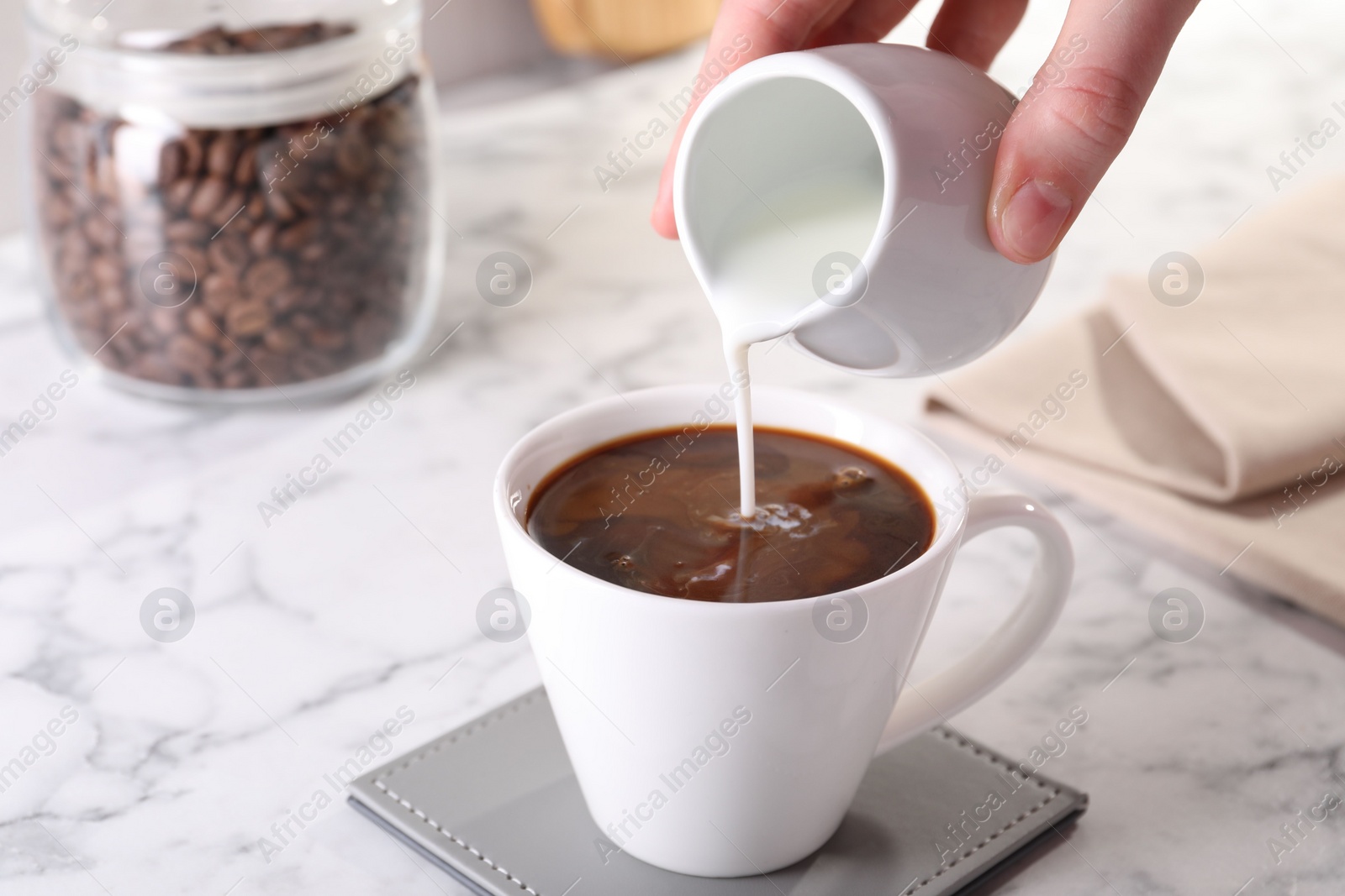 Photo of Woman pouring milk into cup with aromatic coffee at white marble table, closeup