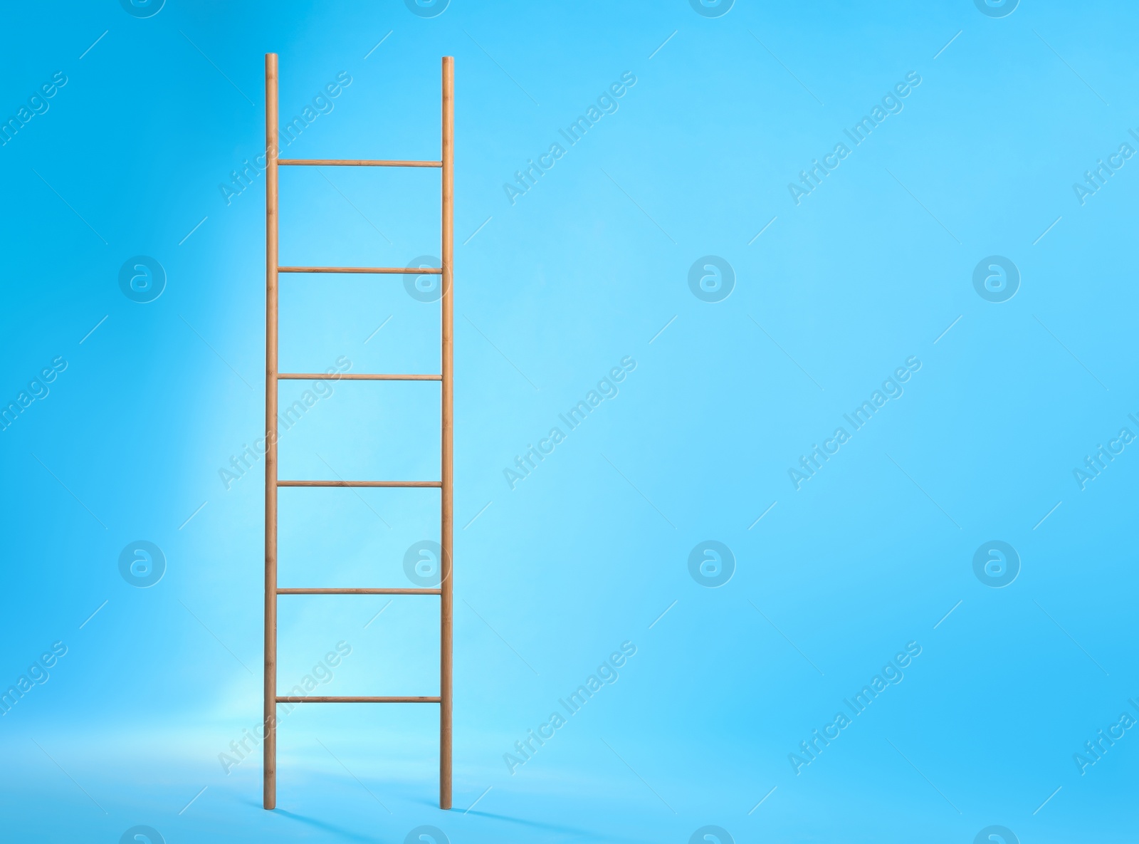 Photo of Modern wooden ladder on light blue background. Space for text