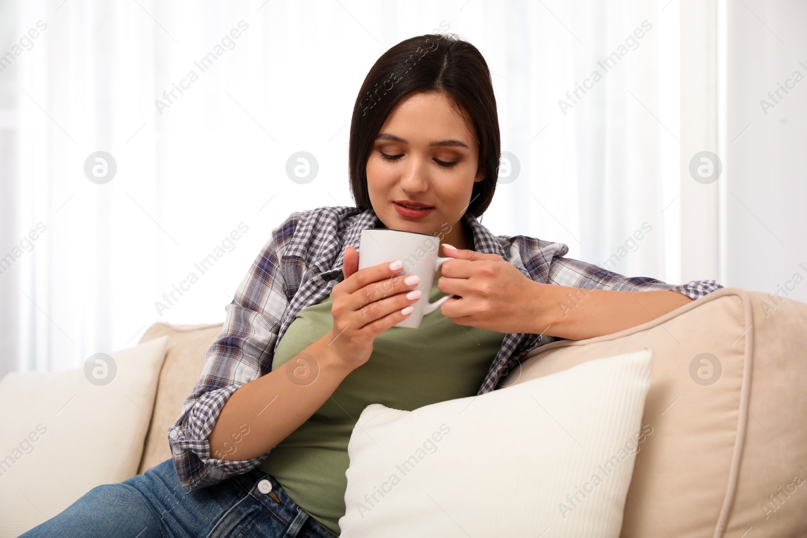 Photo of Young woman with cup of drink relaxing on couch at home