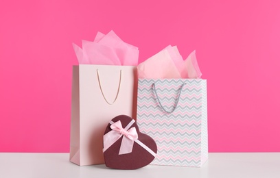 Photo of Gift bags and box on white table against pink background