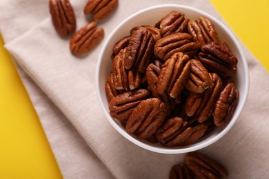 Photo of Bowl with tasty nuts on yellow background, flat lay