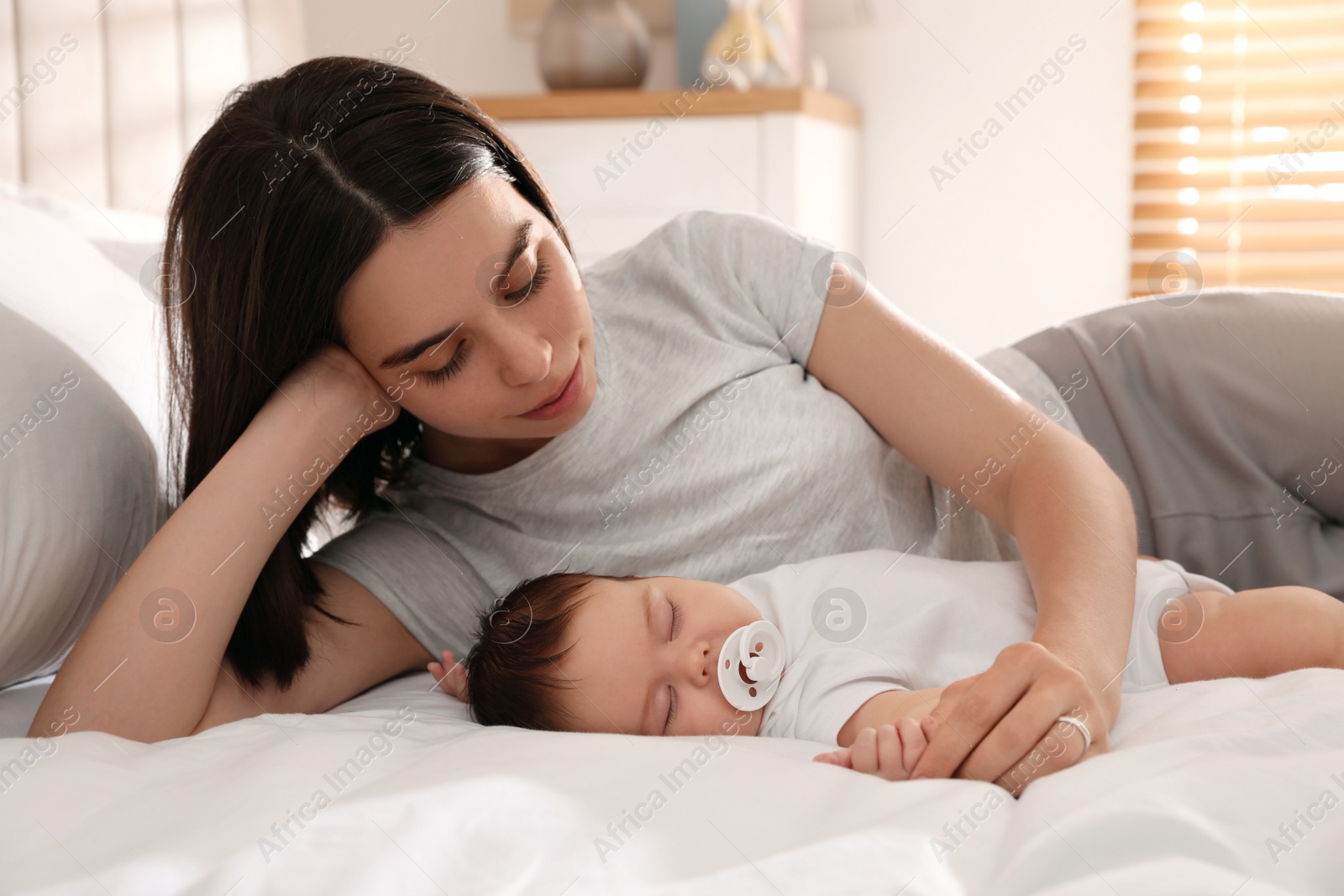 Photo of Young mother resting near her sleeping baby on bed at home