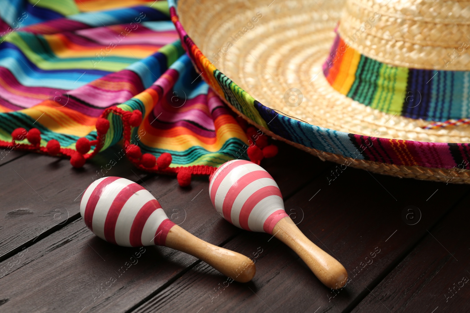 Photo of Mexican sombrero hat, maracas and colorful poncho on wooden background