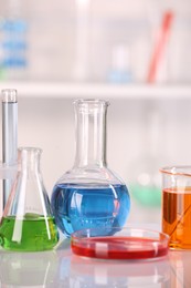 Laboratory analysis. Glass flasks and Petri dish with liquids on white table against blurred background