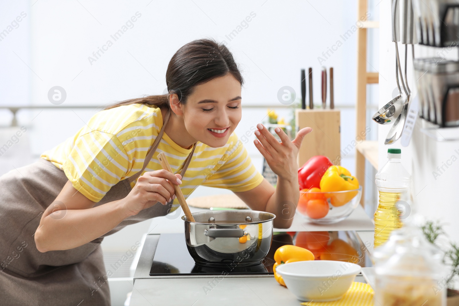 Photo of Young woman cooking tasty soup in kitchen