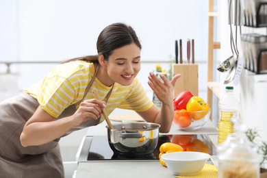 Young woman cooking tasty soup in kitchen