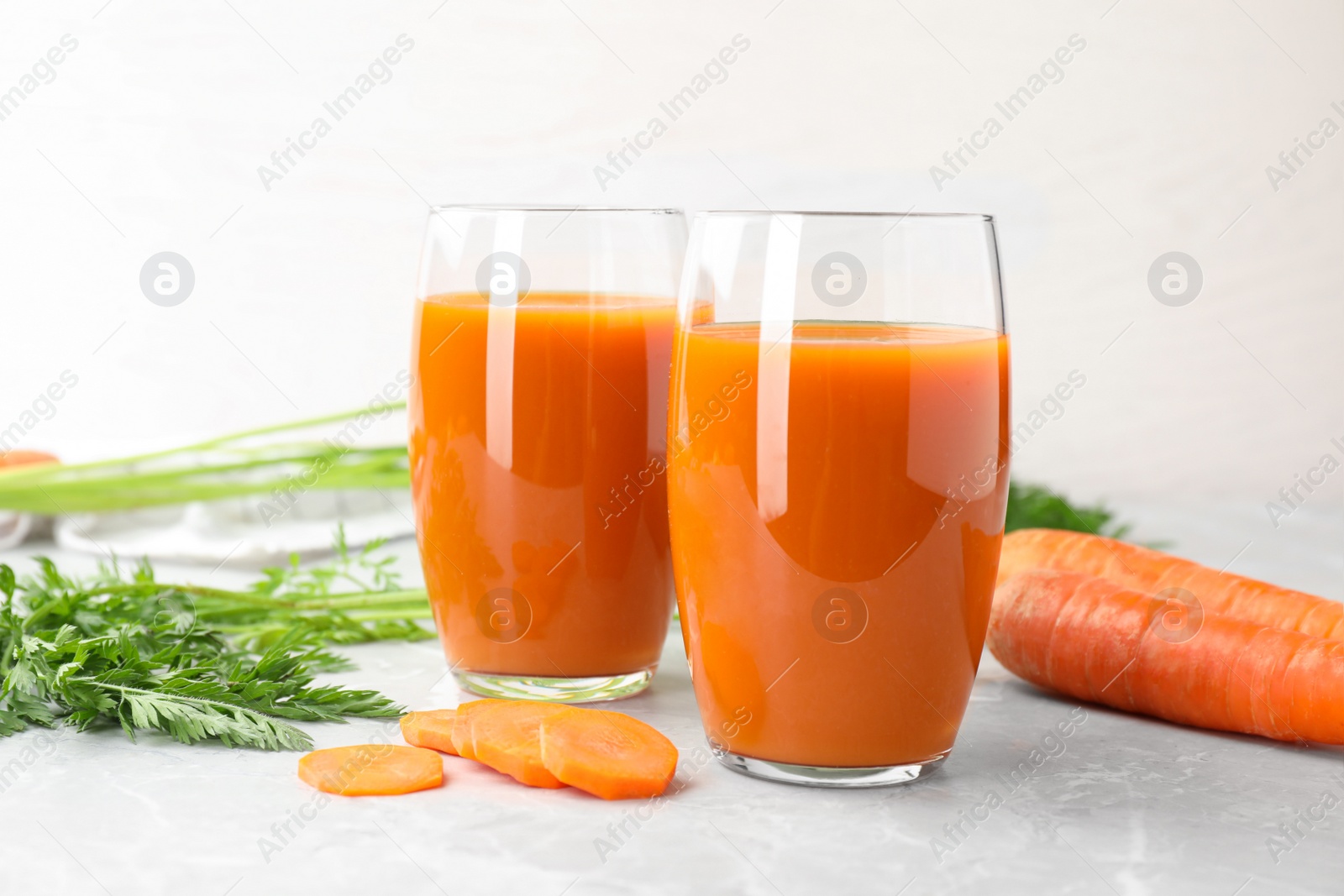 Photo of Glasses of drink and carrots on light table, space for text