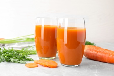 Glasses of drink and carrots on light table, space for text