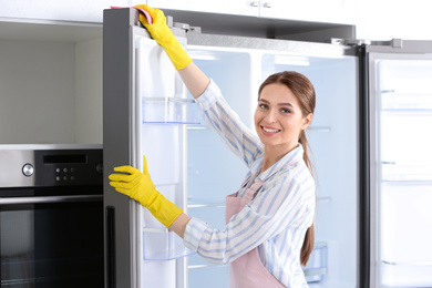 Woman in rubber gloves cleaning refrigerator at home