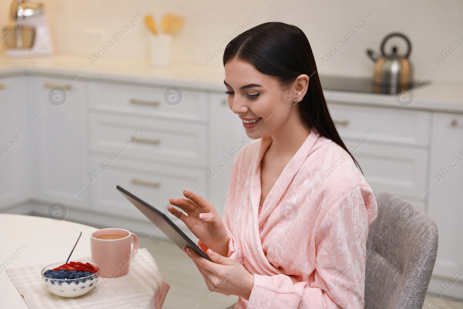 Photo of Young woman with tablet having breakfast in kitchen. Morning routine