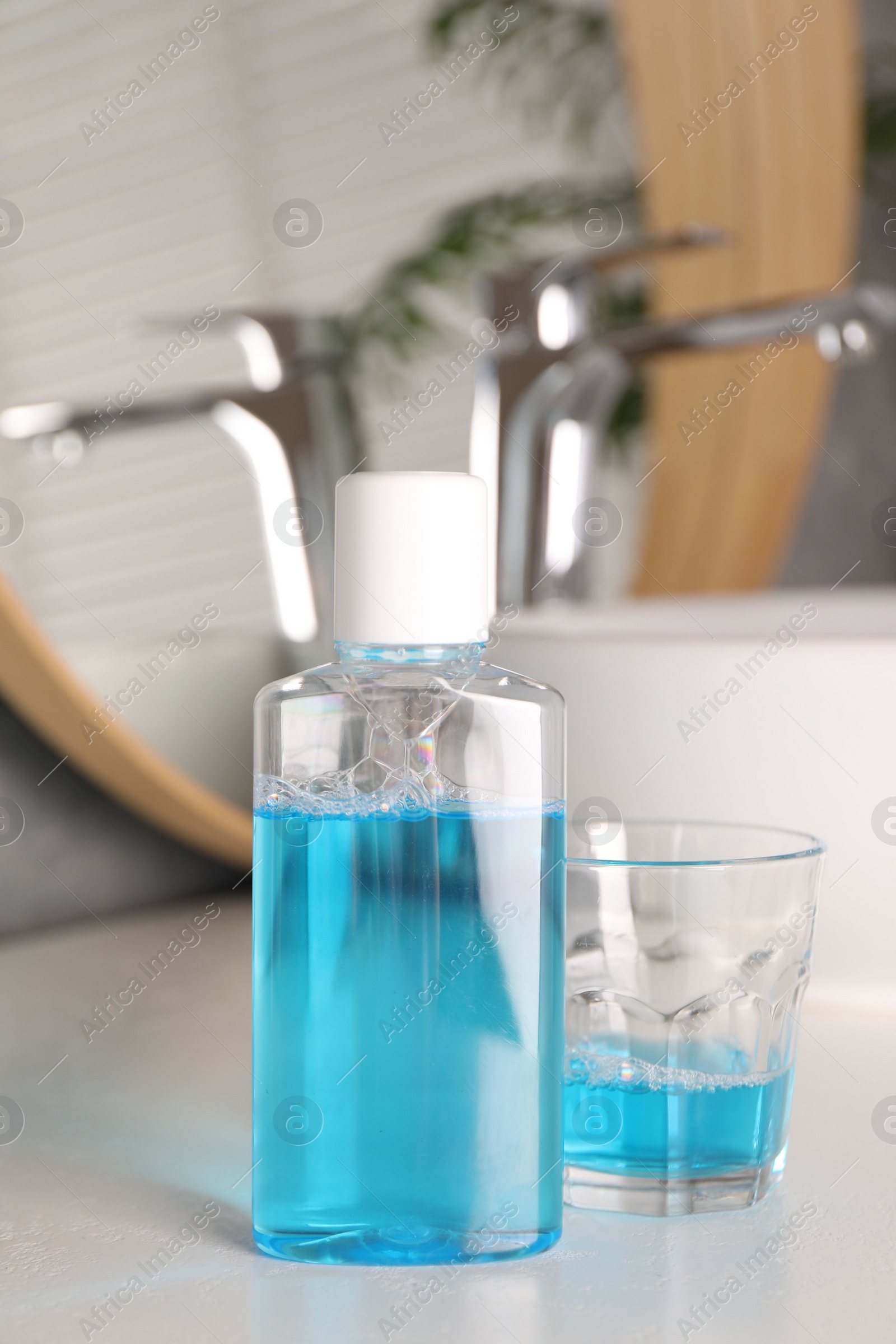 Photo of Bottle and glass of mouthwash on white countertop in bathroom