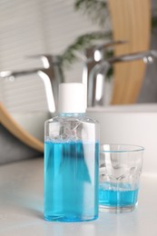 Bottle and glass of mouthwash on white countertop in bathroom