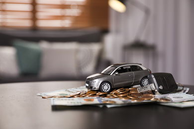 Photo of Miniature automobile model, key and money on table indoors. Car buying