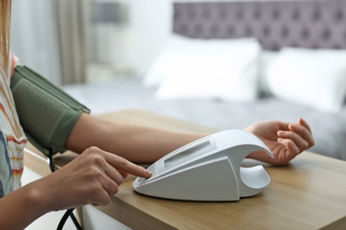 Woman checking blood pressure with sphygmomanometer at table indoors, closeup. Cardiology concept