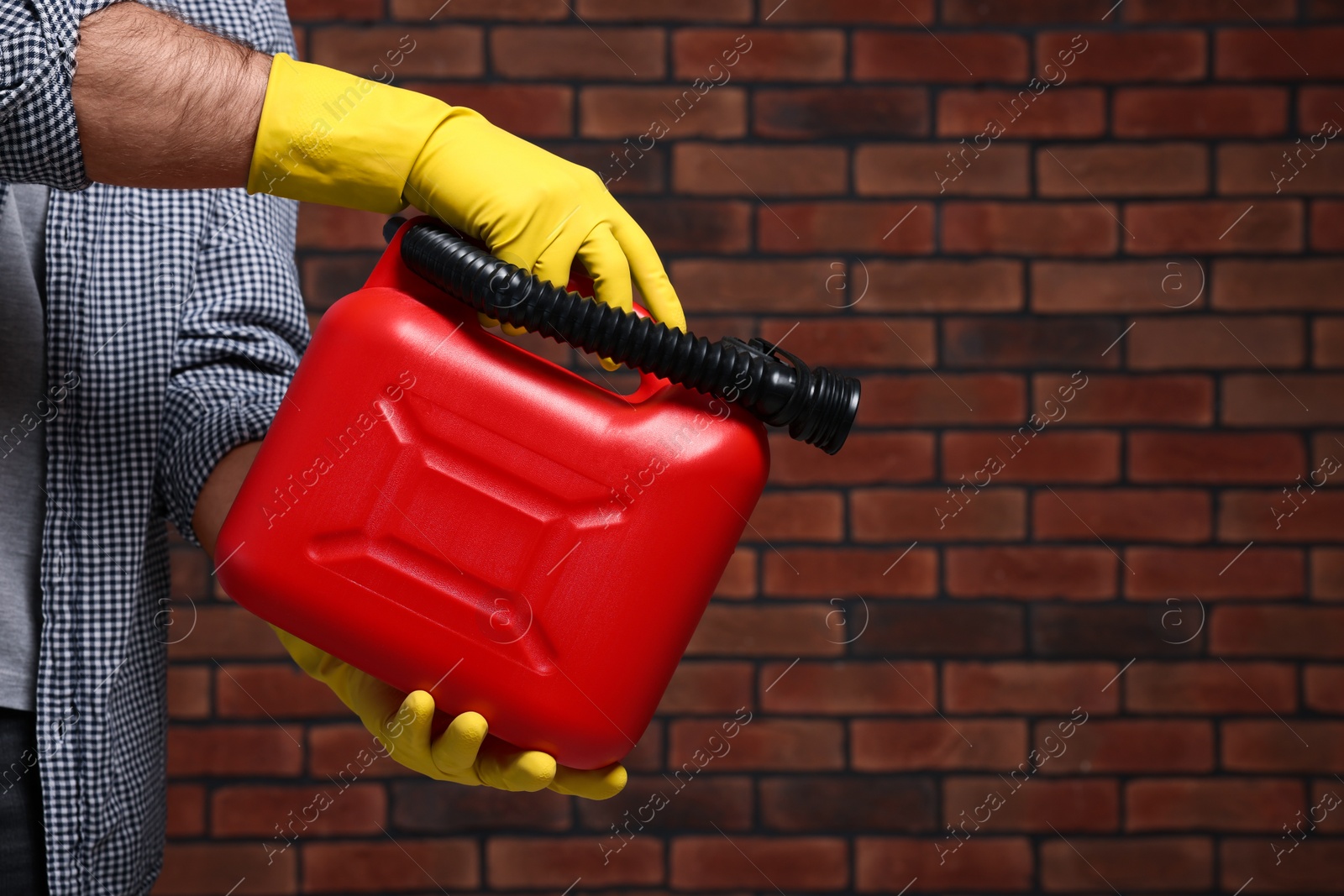 Photo of Man holding red canister against brick wall, closeup. Space for text