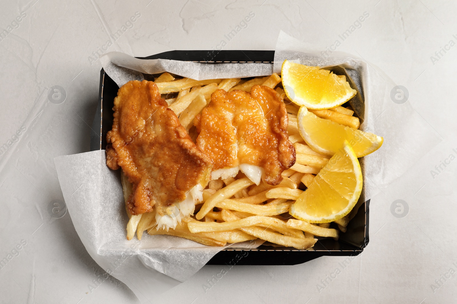 Photo of Container with British traditional fish and potato chips on light background, top view