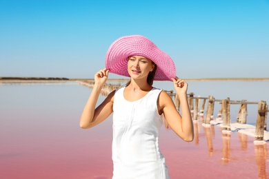 Beautiful woman with hat posing near pink lake on summer day