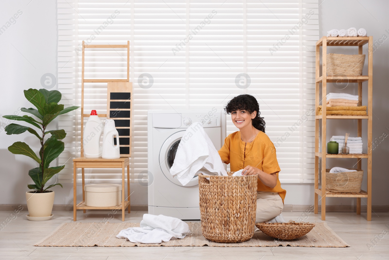 Photo of Happy woman with laundry near washing machine indoors