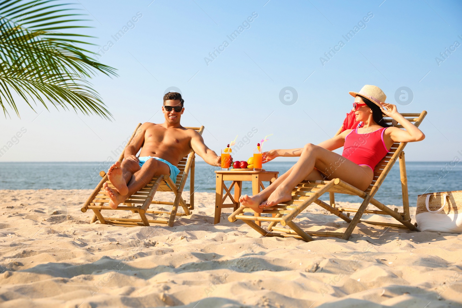 Photo of Couple with drinks resting on sunny beach at resort