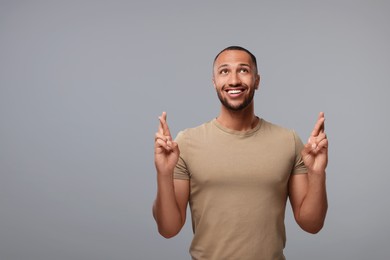 Photo of Happy man crossing his fingers on grey background, space for text