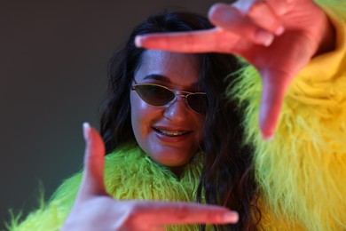 Portrait of beautiful woman in yellow fur coat and sunglasses posing on dark background with neon lights