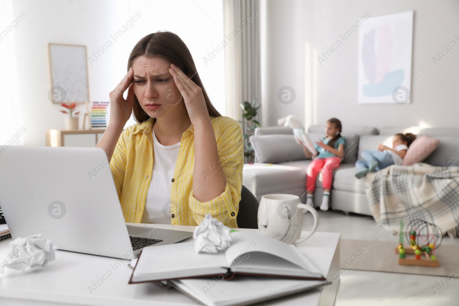 Photo of Children disturbing stressed woman in living room. Working from home during quarantine