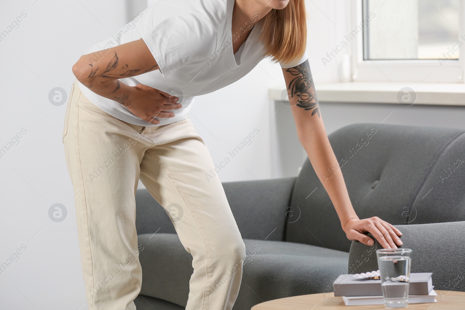 Photo of Young woman suffering from menstrual pain near sofa indoors, closeup