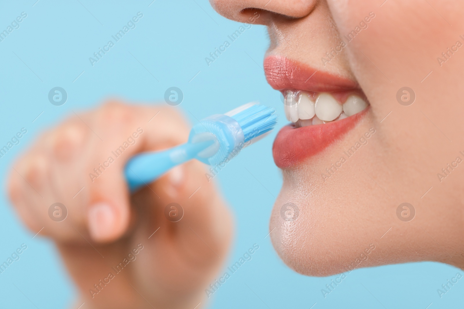 Photo of Woman brushing her teeth with plastic toothbrush on light blue background, closeup