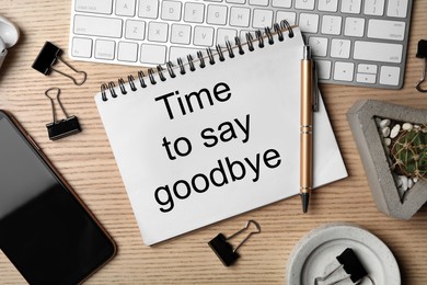 Image of Notebook with text Time to say goodbye, keyboard and smartphone on wooden table, flat lay