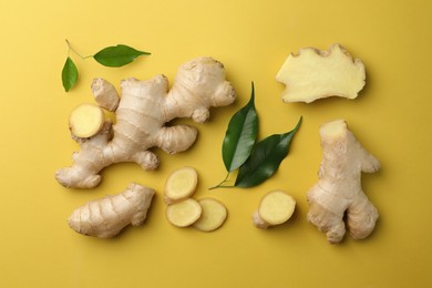 Photo of Fresh ginger with green leaves on pale light yellow background, flat lay