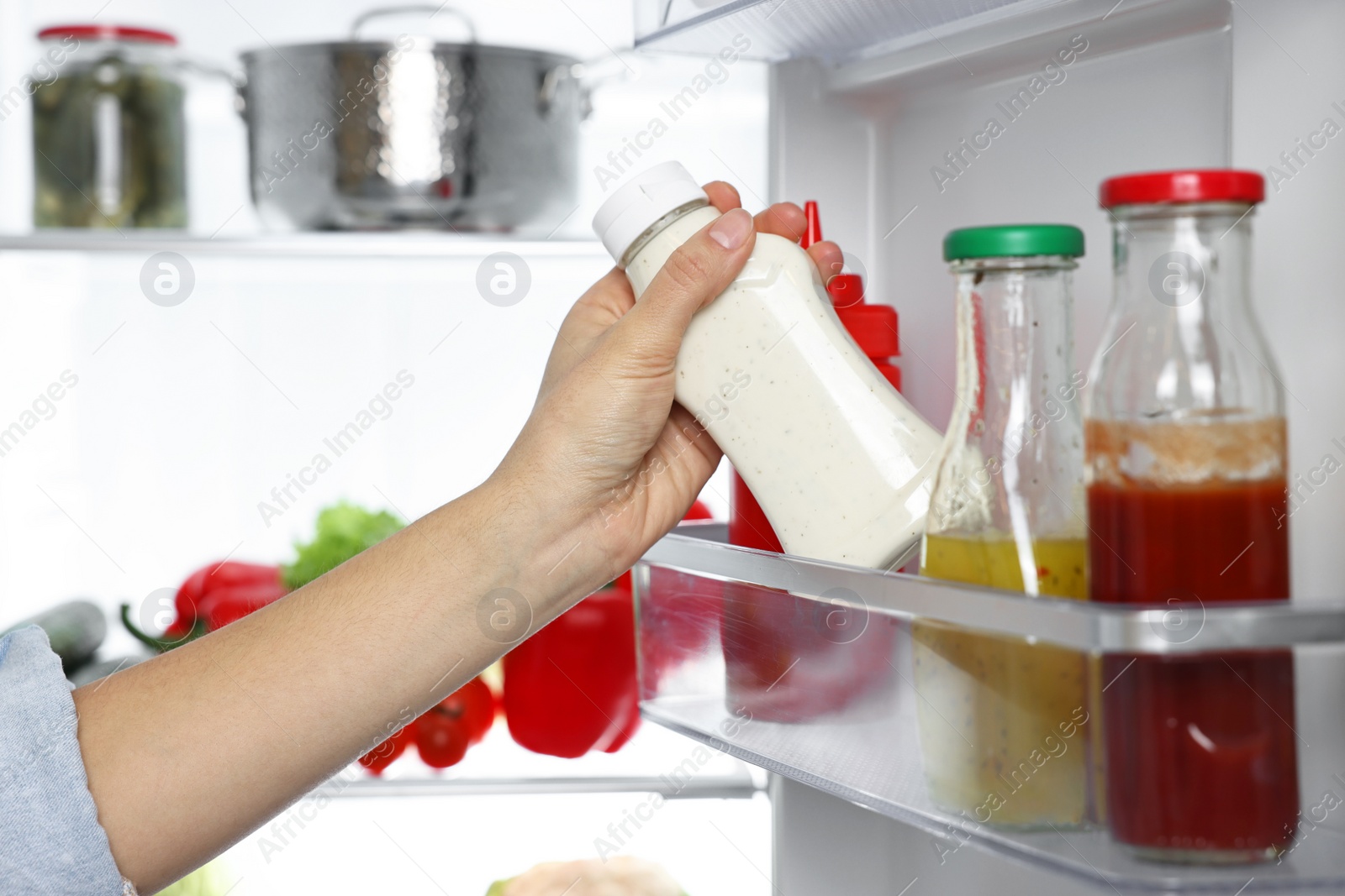 Photo of Young woman taking bottle of sauce out of refrigerator, closeup