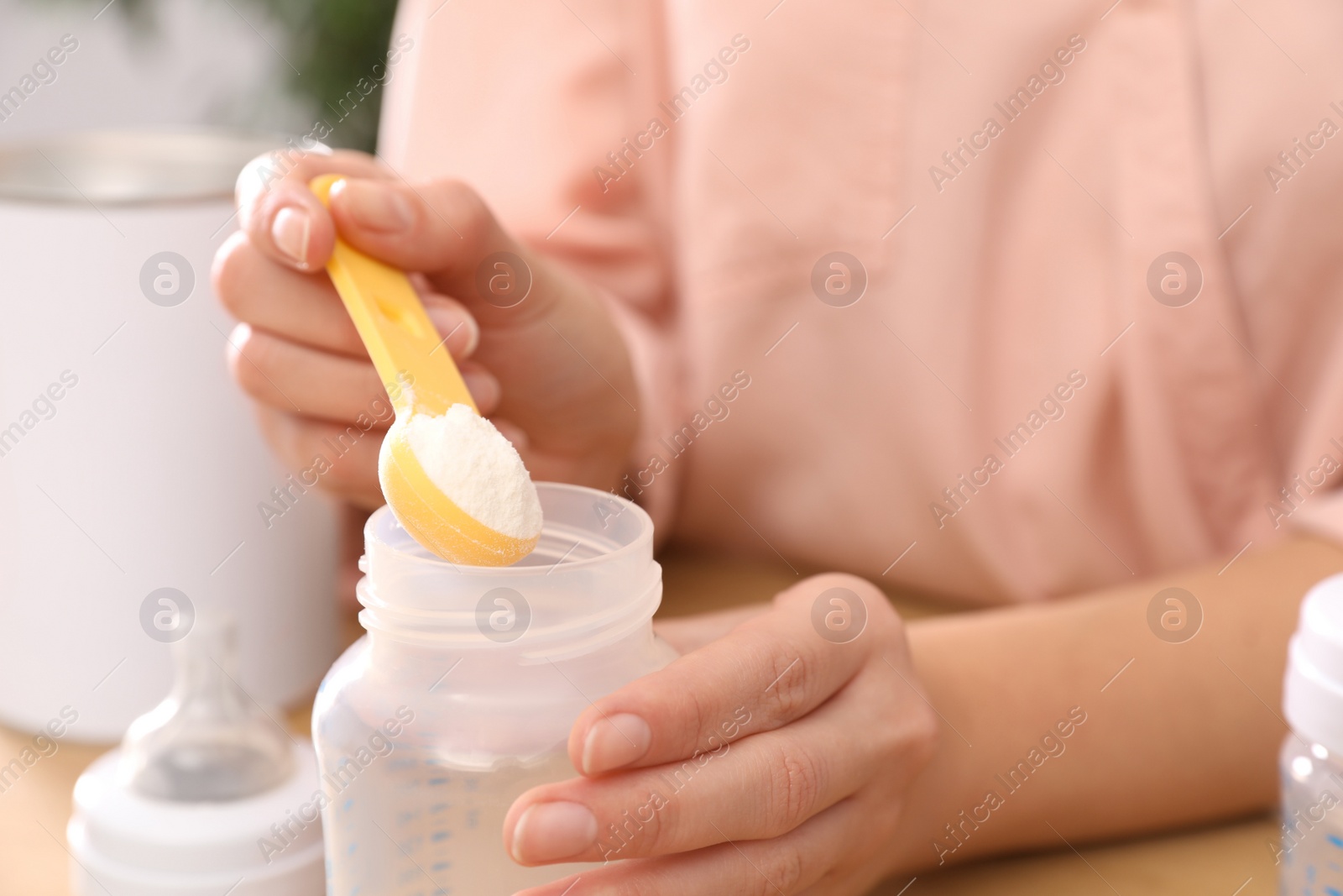 Photo of Woman preparing infant formula at table, closeup. Baby milk